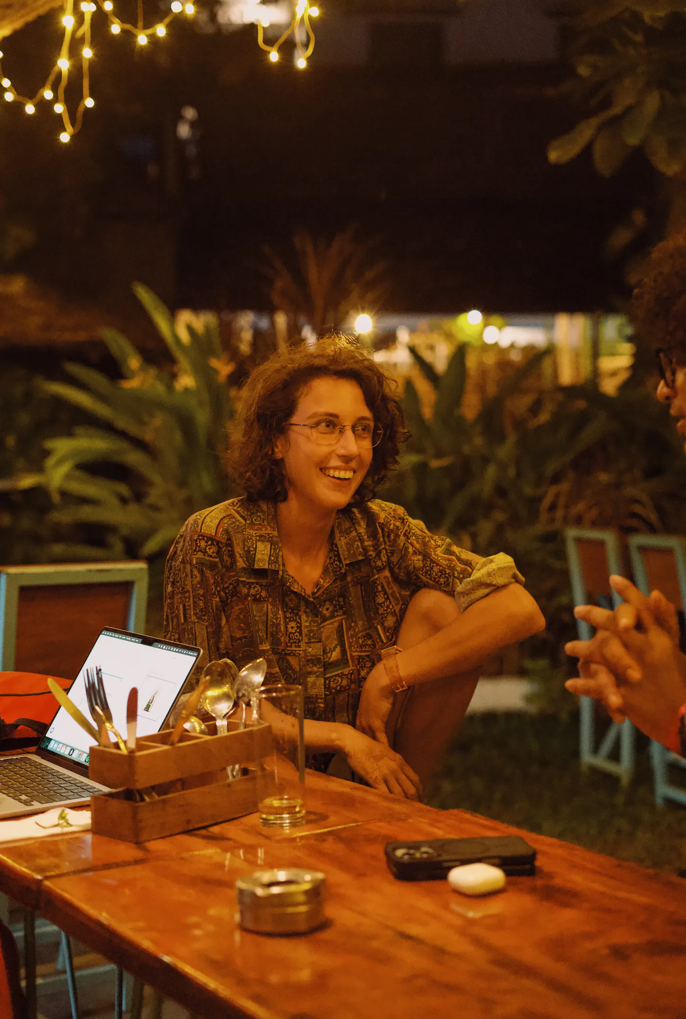 Guests talking around a café table beneath evening lights