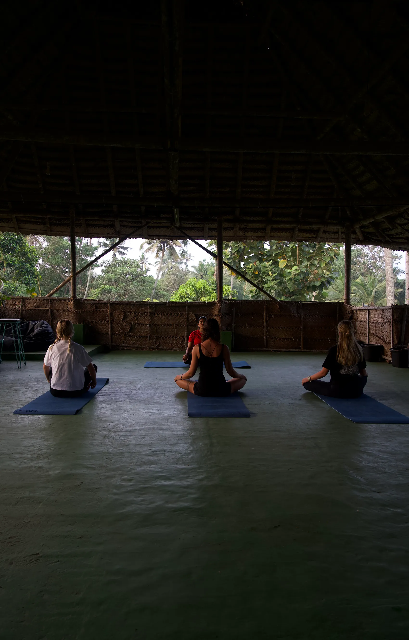 A small yoga group seated on mats in an open-sided hall